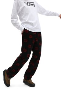 Pantalon noir avec un motif floral rouge, associé à une chemise blanche à manches longues et des baskets marron à semelles noires.