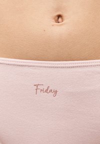 Κοντινό πλάνο του κάτω μέρους της κοιλιάς ενός ατόμου που φοράει ροζ ύφασμα με την λέξη „Friday“ τυπωμένη πάνω από τη μέση.