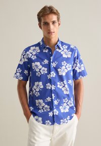 Camisa de botones de manga corta azul con estampado floral de hibisco blanco, hecha de tela ligera, con cuello y cierre de botones.