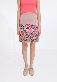 Jupe en tricot rose avec un motif floral aux couleurs vives, associée à un haut sans manches corail et des chaussures beige à bout rond.