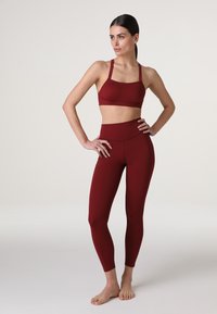 Set di reggiseno sportivo e leggings color bordeaux realizzato in un materiale liscio e elasticizzato, con una vestibilità aderente e cuciture minime per garantire comfort.