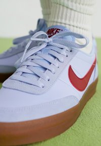 Lyseblå sneakers med rød Nike swoosh, snørelukning og tekstureret overflade. Gummisål i naturgummi og polstret krave med synlig hvid sok.