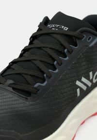 Chaussure de course noire avec une tige texturée, des lacets plats et une semelle intermédiaire légère avec un accent blanc sur le côté et un détail de semelle extérieure rouge.