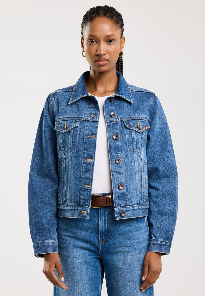 Jeans jakna v svetlo modri barvi z gumbi, prsni žepi in klasičnim ovratnikom. Nosi se čez belo majico, v kombinaciji z modrimi džins hlačami.