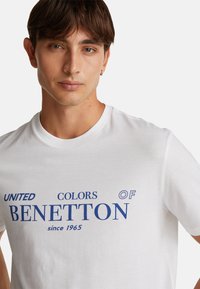 Bílá bavlněná tričko s modrým potiskem "UNITED COLORS OF BENETTON since 1965" a klasickým kulatým výstřihem.