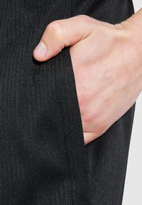 Schwarzer gerippter Stoff mit einer sichtbaren Tasche und einer eingefügten Hand, die die glatte Textur und das strukturierte Design zeigt.