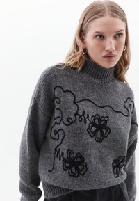 Maglione grigio lavorato a maglia con colletto alto, caratterizzato da ricami floreali neri e linee sinuose. Tessuto testurizzato con vestibilità morbida.