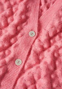 Pink knitted cardigan featuring textured bobble pattern, ribbed edges, and three large white buttons along the front. Soft, fluffy material.