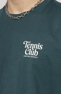 Tamsiai mėlynos spalvos trumpomis rankovėmis marškinėliai su baltais užrašais "Tennis Club" ir "KAOTIKO SOCIETY". Audinys yra lygus, o iškirpė - apvali.
