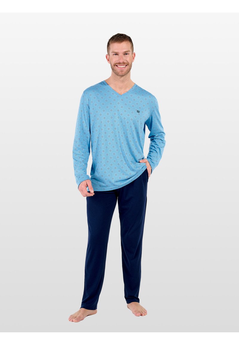 Camicia a maniche lunghe azzurro chiaro con scollo a V e una texture a motivi, abbinata a pantaloni del pigiama blu scuro. Il modello è in piedi a piedi nudi, sorridente.