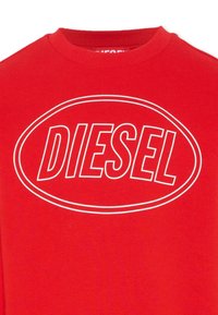 Czerwony bawełniany sweter z dużym białym owalem, na którym widnieje napis "DIESEL" w wyraźnej, pogrubionej czcionce.
