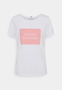 Camiseta de algodón blanca con un gráfico rectangular rosa con "TOMMY HILFIGER" impreso en blanco. Cuello redondo y mangas cortas.