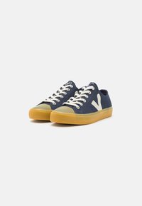 Navy canvas sneakers with beige laces and a beige rubber toe cap. Features a white logo on the side and a light brown rubber outsole.
