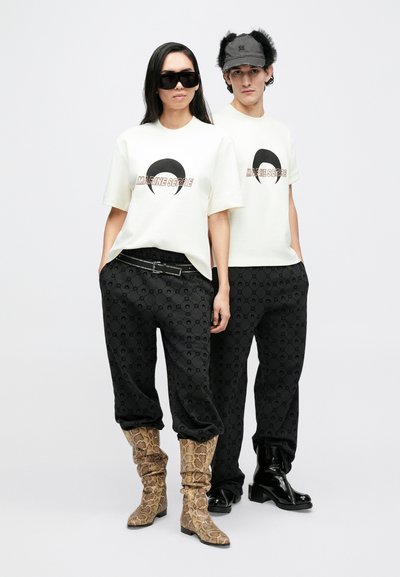 Cream t-shirts with black graphics, paired with black patterned pants. One model wears snake print boots; the other has shiny black footwear.