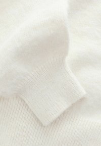 Light cream wool sweater with ribbed cuffs, featuring a soft texture and smooth finish, showcasing subtle variations in color.