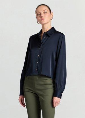 Marineblaue Satin-Bluse mit Knöpfen, Kragen, kurzem Schnitt, langen Ärmeln und goldfarbenen Knöpfen. Kombiniert mit olivgrünen, enganliegenden Hosen.