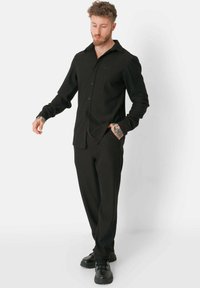 Zwarte button-up shirt met een gestructureerd oppervlak, gecombineerd met bijpassende broeken en zwarte schoenen. Heeft een ontspannen pasvorm en lange mouwen.
