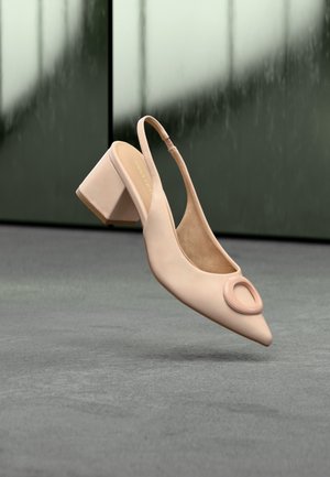 Beżowe szpilki typu slingback z okrągłą ozdobną klamrą na spiczastym nosku, pokazane na rozmytym tle.