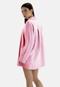 Roze, gestructureerd shirt met een losse pasvorm, lange mouwen en een rugpas. De stof heeft een gerimpelde uitstraling. Voorzien van een kraag en knoopsluiting.