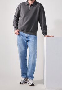 Pullover grigio con zip e colletto, abbinato a jeans azzurri e scarpe sportive argento. Tessuto strutturato e design a gamba dritta.