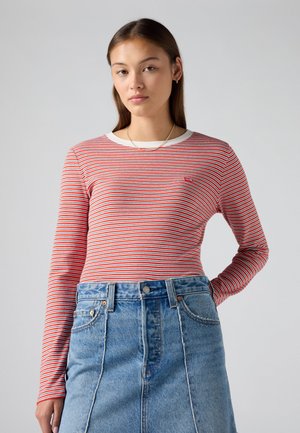 Camicia di cotone a maniche lunghe rossa e bianca a righe con scollatura a girocollo, abbinata a una gonna di jeans blu a vita alta con cuciture frontali.