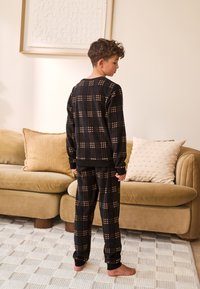 Sort ternet pyjamasæt i blødt materiale med rund halsudskæring og elastiske manchetter. Designet indeholder lyse beige tern.