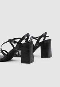 Sandalias de tacón negro con un diseño de imitación de cuero texturizado, que cuentan con un tacón grueso y múltiples correas entrelazadas para mayor soporte.