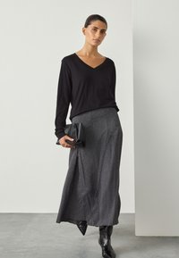 Czarna bluzka z długim rękawem i dekoltem w serek, zestawiona z szarą, błyszczącą długą spódnicą maxi oraz czarnymi kozakami z noskiem w szpic; trzyma czarną kopertówkę. Detale z fakturowanej tkaniny.