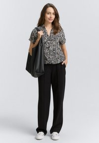 Top a maniche corte bianco e nero con colletto, abbinato a pantaloni neri a gamba larga e sneakers bianche. Porta con sé una grande borsa nera.