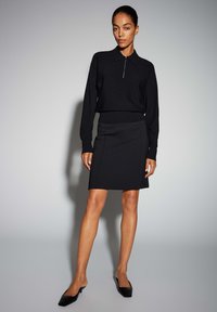 Pull-over en maille noire avec col et fermeture éclair, associé à une jupe noire mi-longue. Design simple et épuré, avec un minimum de quincaillerie.