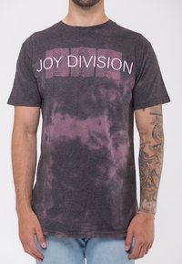 Dark gray T-shirt with pink "JOY DIVISION" text and a tie-dye pattern in shades of gray and purple. Short sleeves and crew neck design.