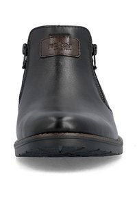 Vue de face d'une botte cheville en cuir noir avec semelle en caoutchouc et étiquette en cuir marron sur la partie supérieure.
