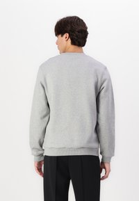 Grå genser laget av mykt stoff, med rund hals og ribbestrikkede mansjetter. Designet er enkelt og rettskåret, vist fra bak.