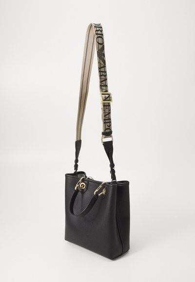 Borsa a tracolla nera in pelle con hardware dorato, manici superiori doppi e una tracolla beige rimovibile con testo logo nero. Superficie texturizzata.