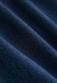 Tamsiai mėlyna džinsinė medžiaga su lygiu tekstūru, pasižyminti matomais įstrižais audimo raštais ir subtiliomis spalvos bei blizgesio variationomis.
