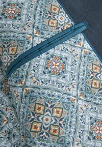 Mustergewebe mit filigranen blauen, grünen und orangefarbenen Designs, die einen leichten Glanz aufweisen. Mit einem soliden türkisfarbenen Rand akzentuiert. Glatte Textur.