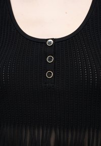 Μαύρο πλεκτό τοπ με ριπ ύφασμα, στρογγυλή λαιμόκοψη και τρία μαύρα κουμπιά με χρυσά περιθώρια στη μέση μπροστά.