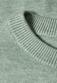 Gros plan d'un pull tricoté vert clair montrant un col rond côtelé et un détail de tissu en maille texturée.