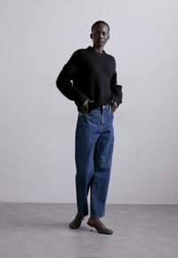 Zwarte fluffy trui, blauw high-waisted jeans met een losse pasvorm, en bruine hoge muiltjes. Eenvoudig, minimalistisch ontwerp met strakke lijnen.