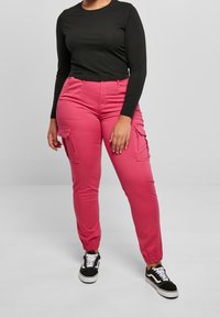 Svart långärmad topp kombinerad med rosa avsmalnande cargobyxor med sidofickor och elastiska mudd, bärs med svart och vita sneakers.