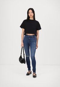 Svart kortärmad t-shirt, blå skinny jeans med slitningar, svarta lägenheter med dekorativa detaljer, och en liten svart handväska.