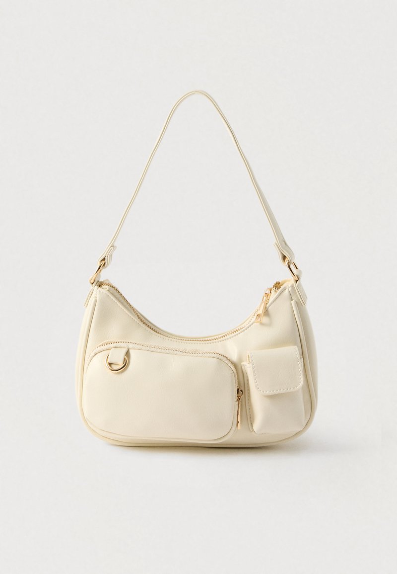 Sac à bandoulière couleur crème avec deux poches avant, l'une avec une fermeture éclair et l'autre avec un rabat, et une bandoulière unique incurvée.