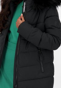 Giacca a vento nera con zip frontale, texture a soffietto e colletto in pelliccia sintetica staccabile. Logo visibile sul colletto e sulla zip laterale.