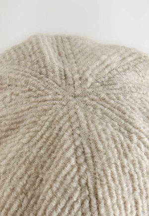 Beige gestrickte Mütze mit einem strukturierten, gerippten Muster. Verfügt über eine runde Krone und dezente Nähte, die eine Naht an der Spitze bilden.
