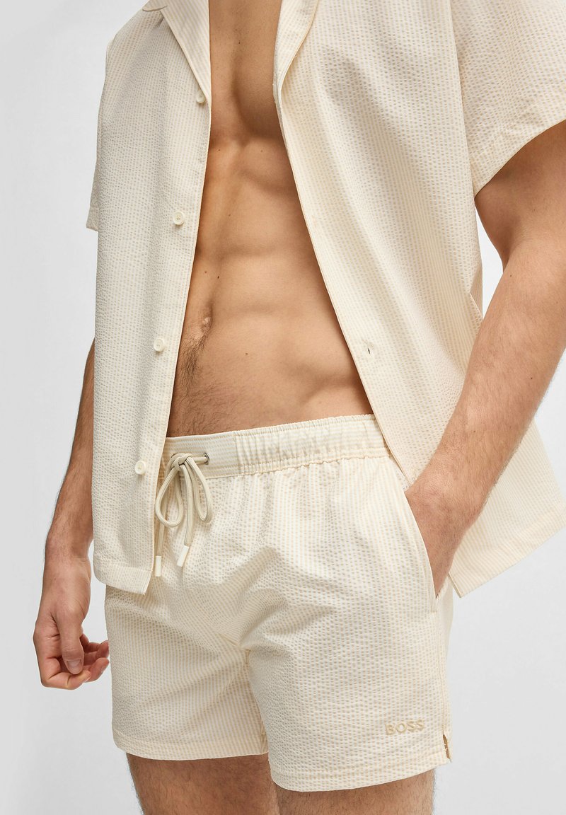 Short-sleeve, light beige shirt and matching shorts with a textured pattern. Drawstring waist with light accents and side pockets.