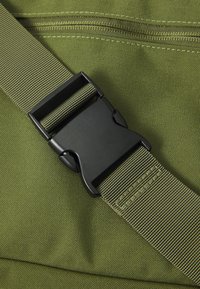 Green fabric strap with a black plastic buckle. The strap features a textured surface and is sewn into the fabric, with visible stitching.