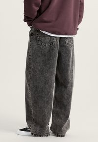 Losse zwarte denim jeans met een vervaagde textuur, voorzien van een vijfvak ontwerp en contrasterend stikwerk, gedragen met zwarte sneakers.