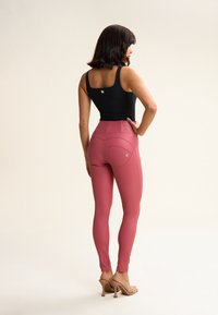 Leggings rosas con una cintura alta y bolsillos traseros; fabricados con material elástico. Combinados con una blusa sin mangas negra y tacones beige.