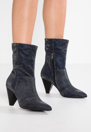 Bottines bleu foncé en tissu brillant et texturé, à bout pointu et talon effilé. Dotées d'une fermeture éclair sur le côté pour un enfilage facile.