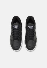 Μαύρα αθλητικά sneakers με δερμάτινο επάνω μέρος, δικτυωτή λεπτομέρεια και λευκή καουτσούκ σόλα. Διαθέτουν στρογγυλά κορδόνια και μινιμαλιστικό σχέδιο.